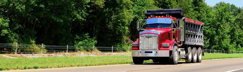 Red heavy-duty dump truck driving on a tree-lined road
