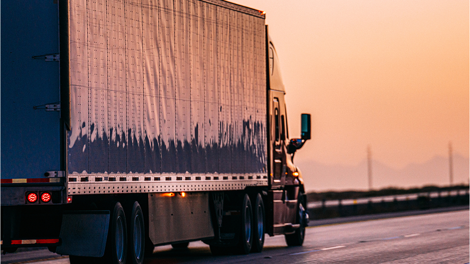 semi truck driving down a highway in the sunset